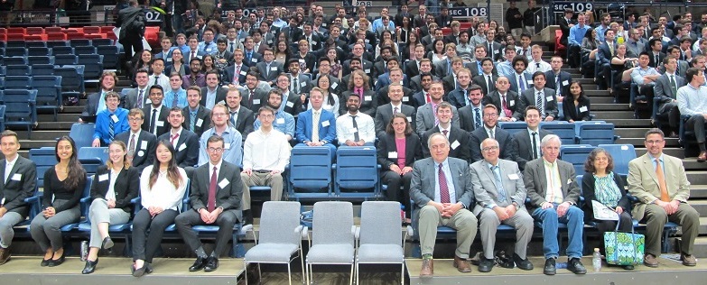 A heartwarming group photo capturing the joyous occasion of successful graduates from a program, all beaming with pride and accomplishment. The graduates, dressed in professional attire, fill the seats of an arena, showcasing a vibrant mix of smiles and enthusiasm. In the foreground, supportive faculty and staff members sit proudly among the graduates, reflecting a shared sense of achievement. The atmosphere is filled with excitement and celebration, encapsulating the hard work and dedication of everyone involved in this milestone moment.