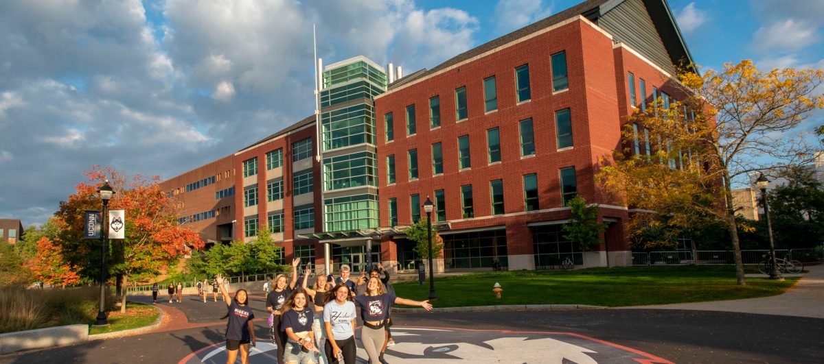 Students outside of the Information Technology Engineering Building smiling and enjoying their day in front of a painted UConn Husky Logo